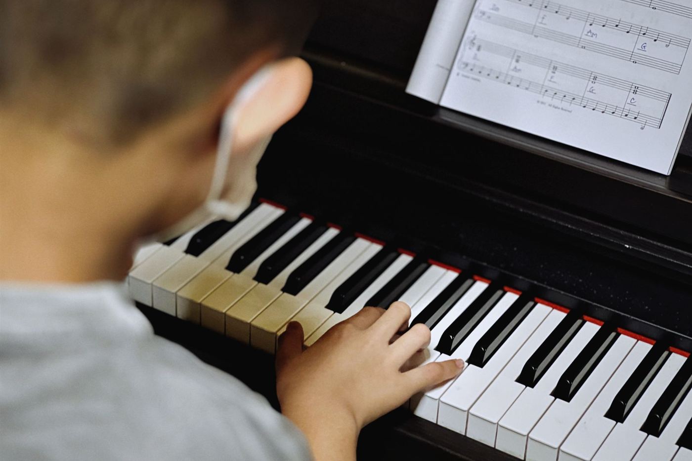 Bé trai luyện tập trên đàn piano cơ với bản nhạc
